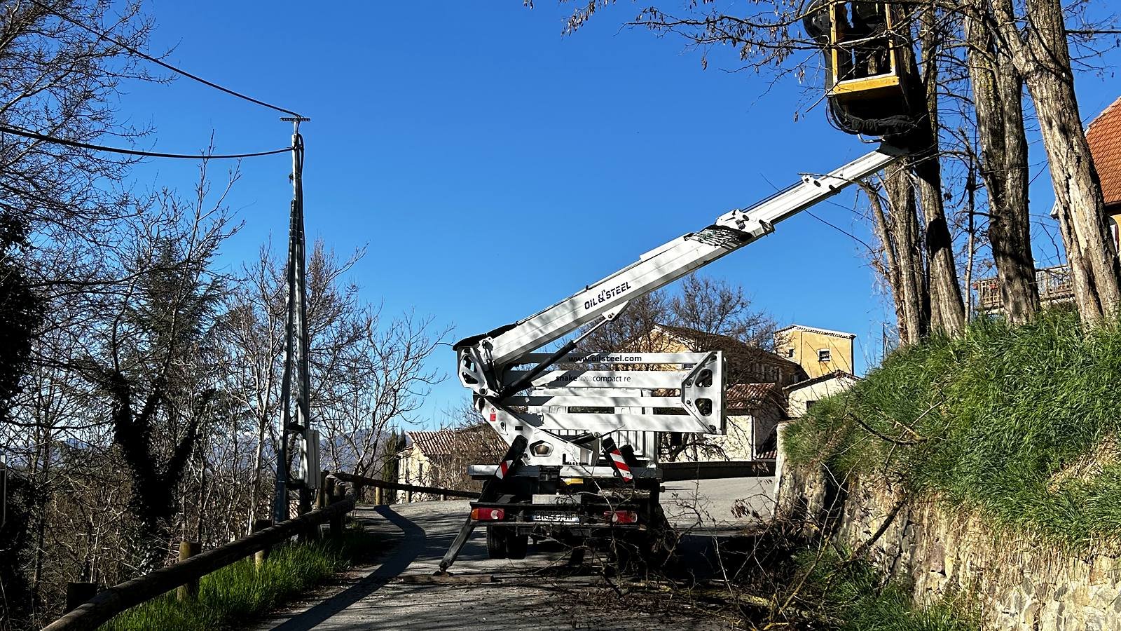 Camion nacelle sur une route de village, nacelle levée dans les arbres